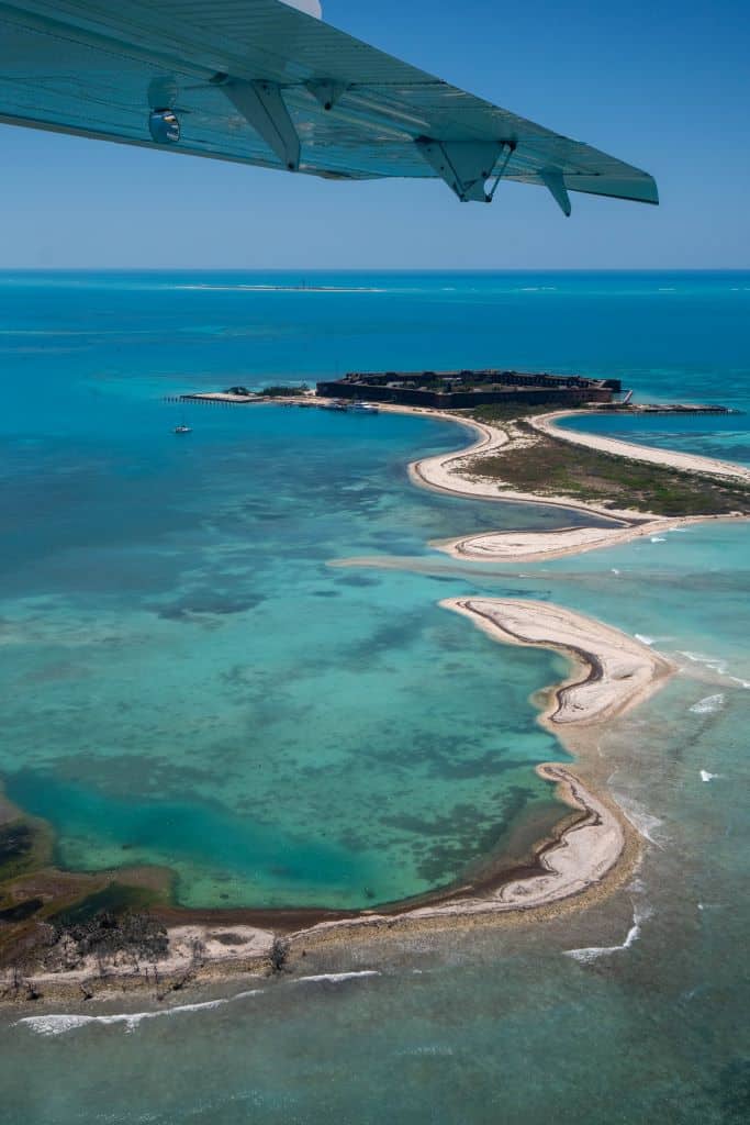 A view looks out the window of a small plane to sandy islands below surrounded by turquoise water in the Dry Tortugas.