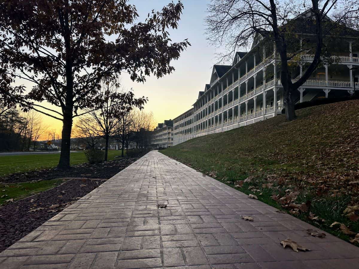 Twilight view of Omni Bedford Springs Resort's historic building, with a brick-lined path leading to its grand white porch, nestled amidst late autumn foliage.