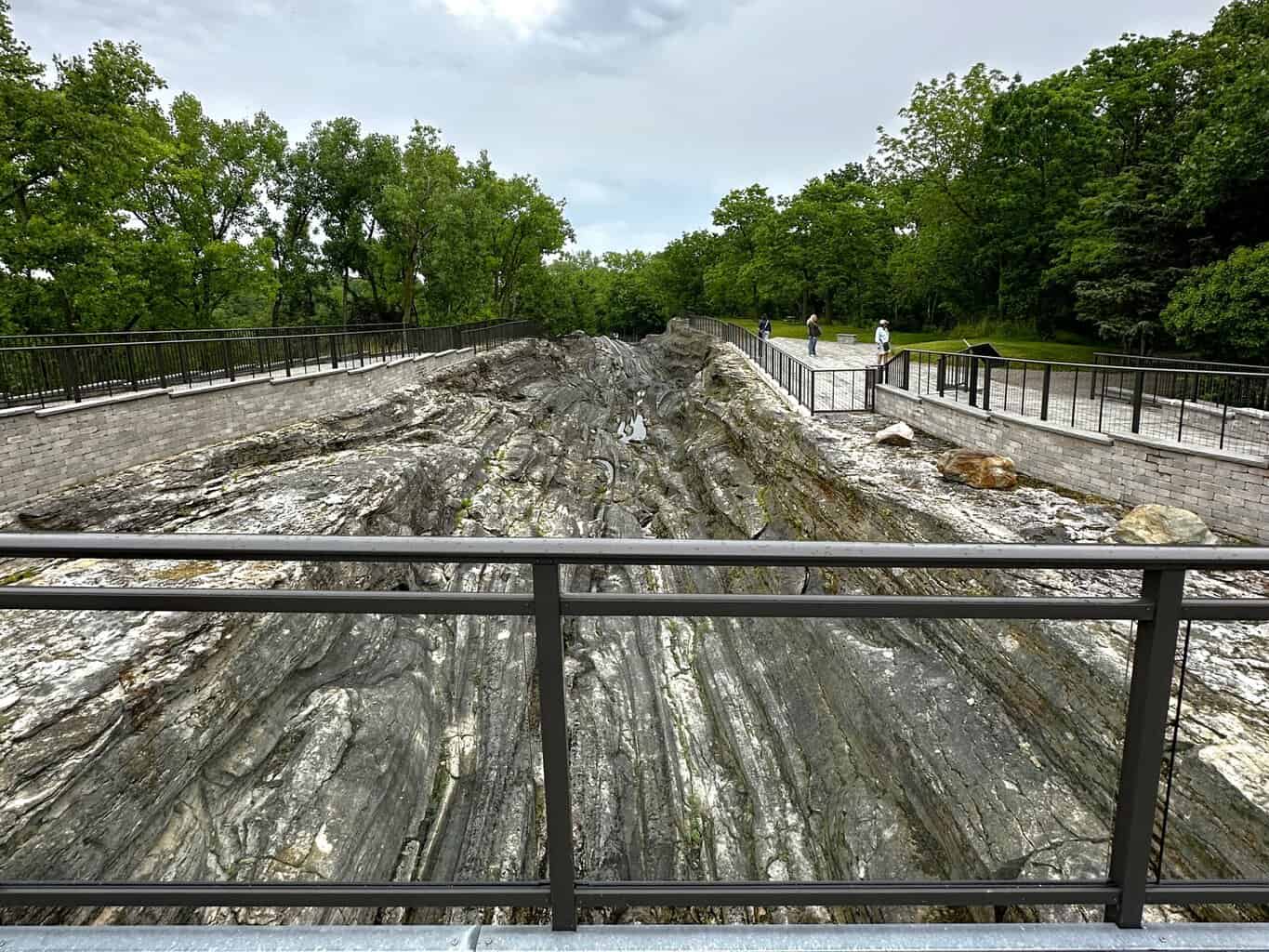 Deep glacial grooves carved into exposed bedrock, surrounded by railings and trees, showcasing one of Kelleys Island’s most famous geological attractions.