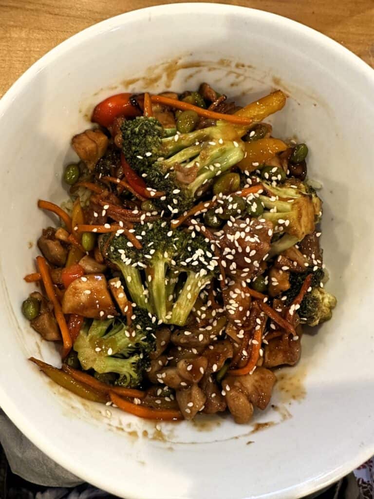 Bowl of stir fried vegetables and chicken with broccoli, carrots, peppers, and edamame topped with sesame seeds. The dish is coated in a glossy savory sauce at Red's Lakehouse in Marblehead, Ohio.