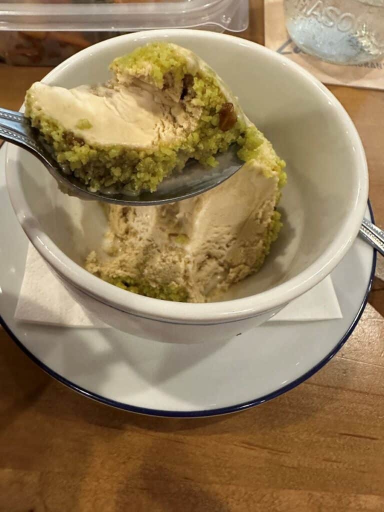 Spoonful of pistachio coated ice cream and lifted above a small bowl showing the layered texture. The dessert combines creamy ice cream with a crumbly green pistachio layer at Red's Lakeside in Marblehead, Ohio.