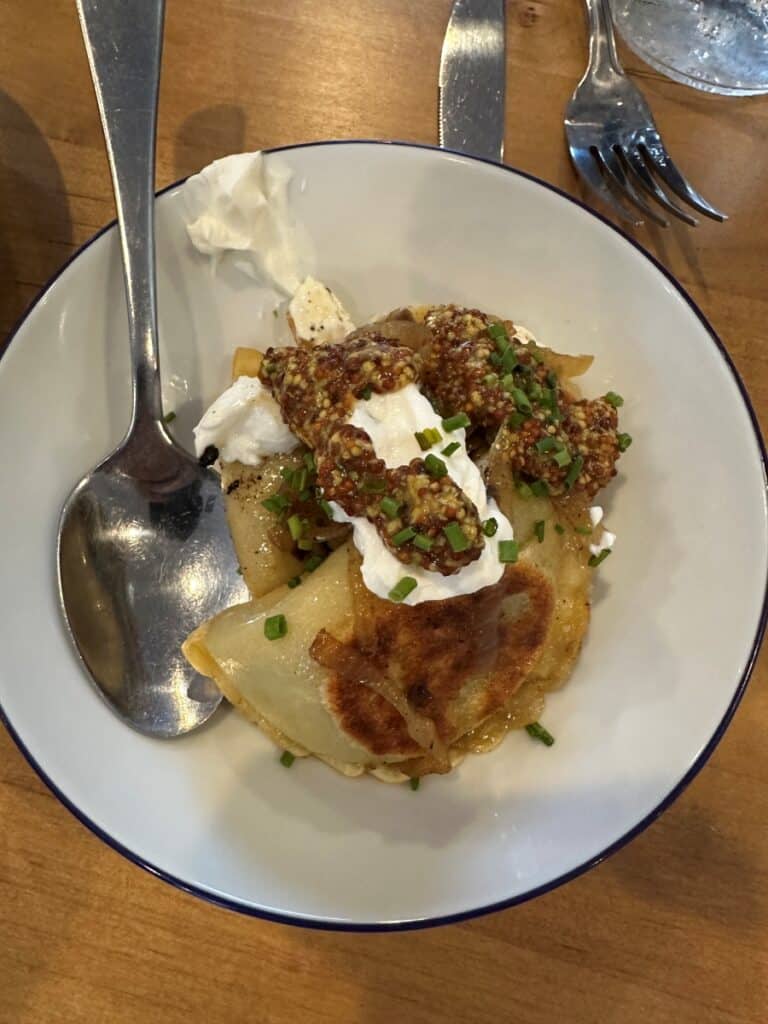 Pan seared pierogis topped with grainy mustard sauce, caramelized onions, and a dollop of sour cream. The savory appetizer is garnished with chopped chives at Red's Lakehouse in Marblehead, Ohio.