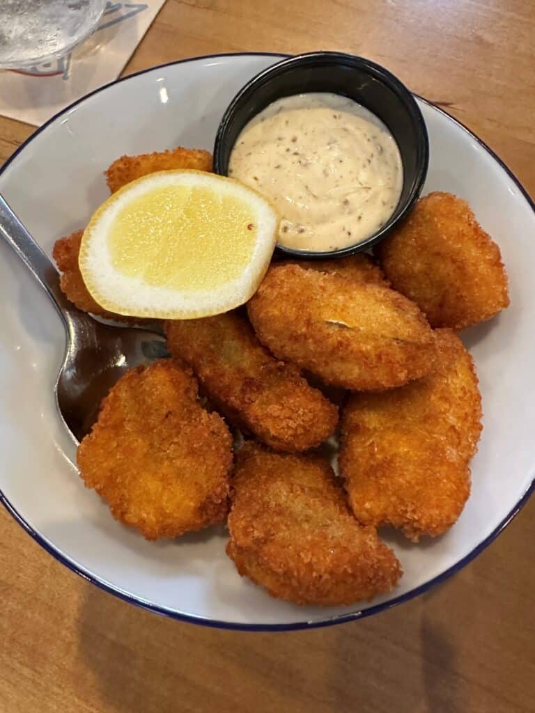 Golden fried walleye bites served with a lemon wedge and a small cup of creamy dipping sauce. The crispy seafood appetizer sits in a white bowl with a spoon at Red's Lakehouse in Marblehead, Ohio.