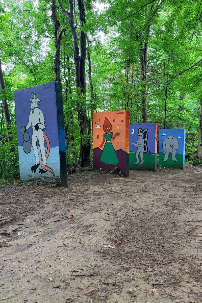 Colorful murals featuring whimsical West Virginia lore characters painted on concrete structures beside a wooded trail at Meeks Mountain in Hurricane, West Virginia.