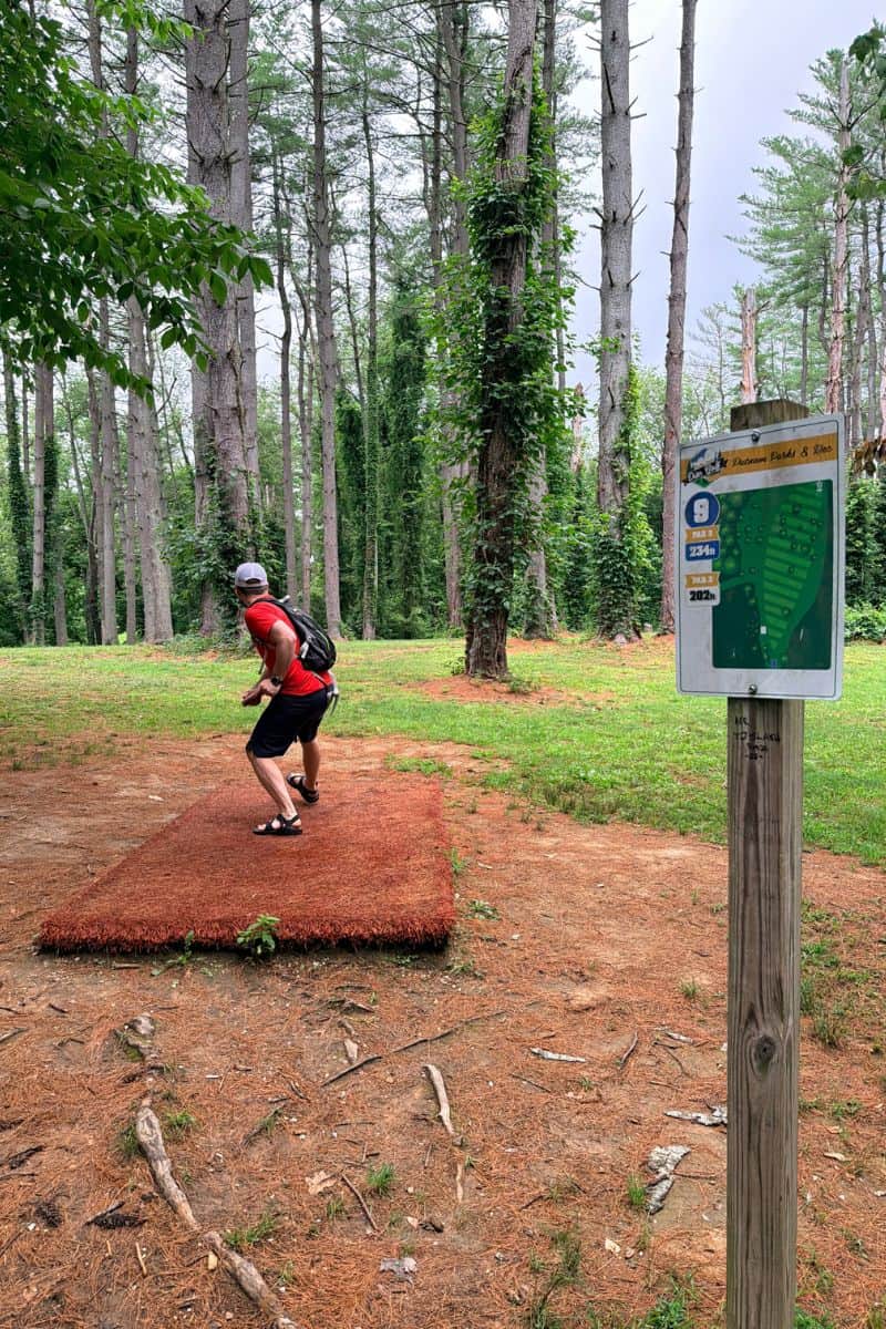 A man throws a disc from the tee for hole nine on the wooded disc golf course at Valley Park in Hurricane, West Virginia.
