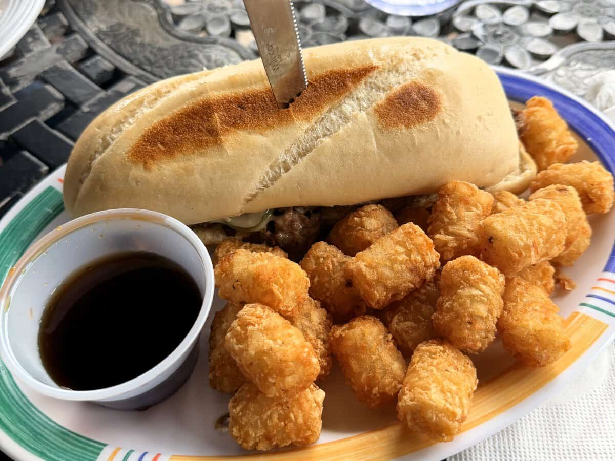 A toasted sandwich with golden tater tots and a cup of dipping sauce on an outdoor table at Coody Brown’s Lakeside Grill in Wolcottville.